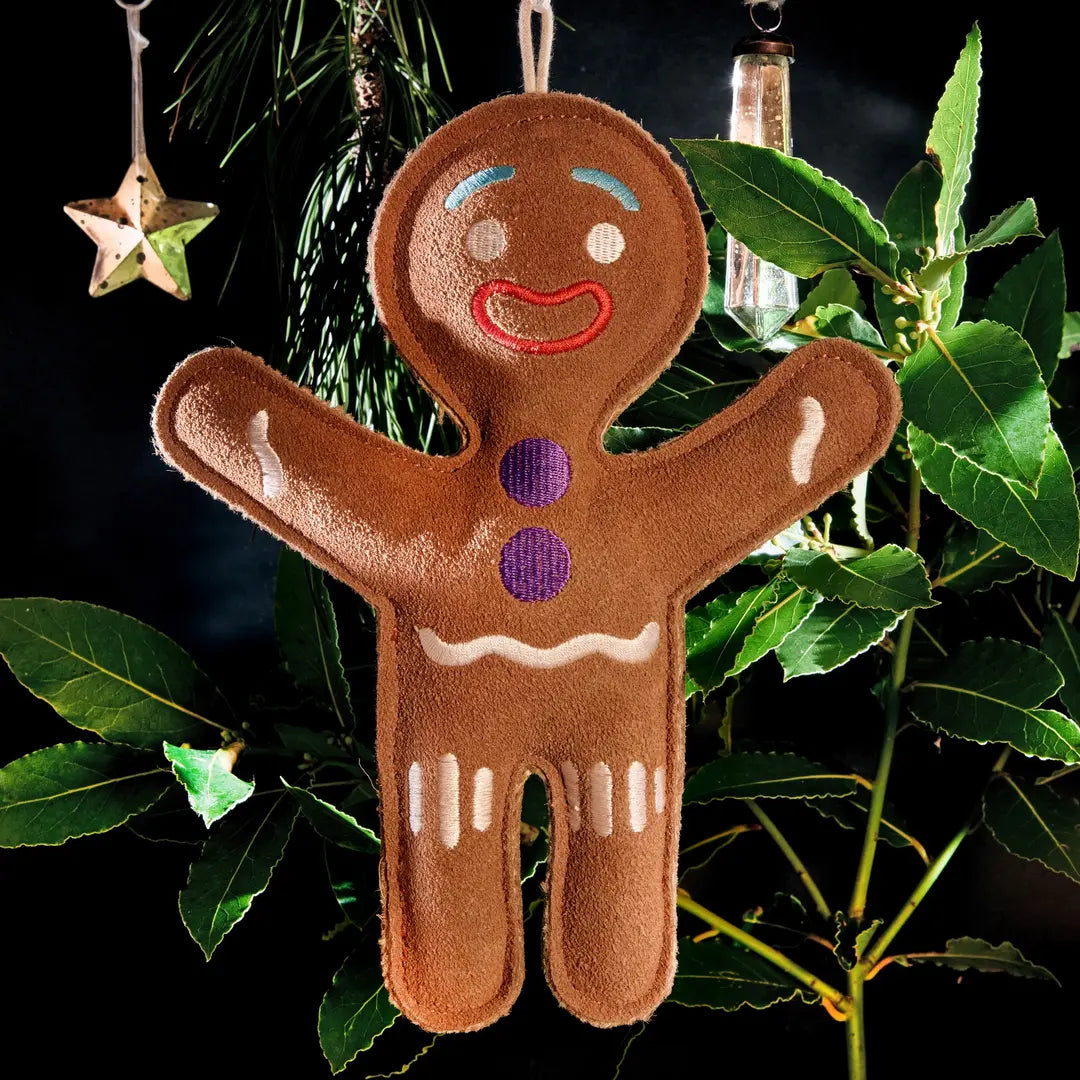 A brown gingerbread person-shaped eco dog toy hanging on a Christmas tree.