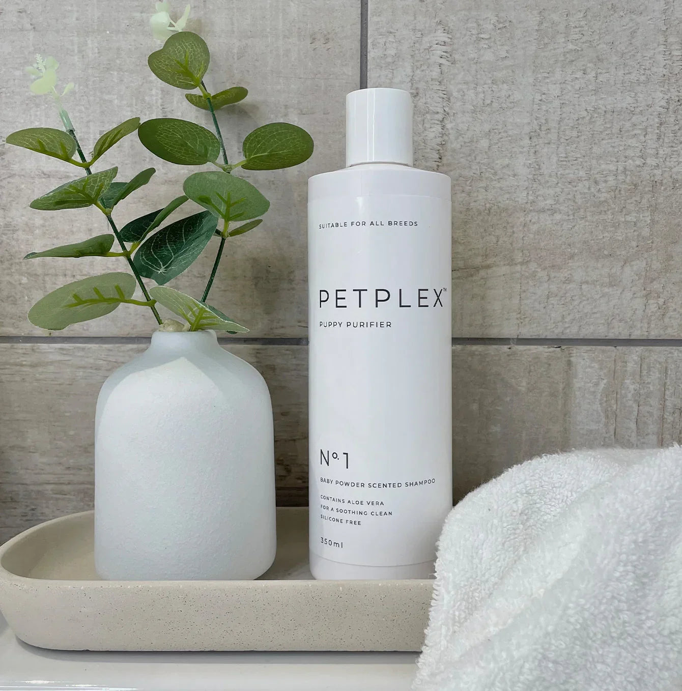 PetPlex No. 1 Puppy Shampoo displayed on a bathroom tray with a towel and decorative vase