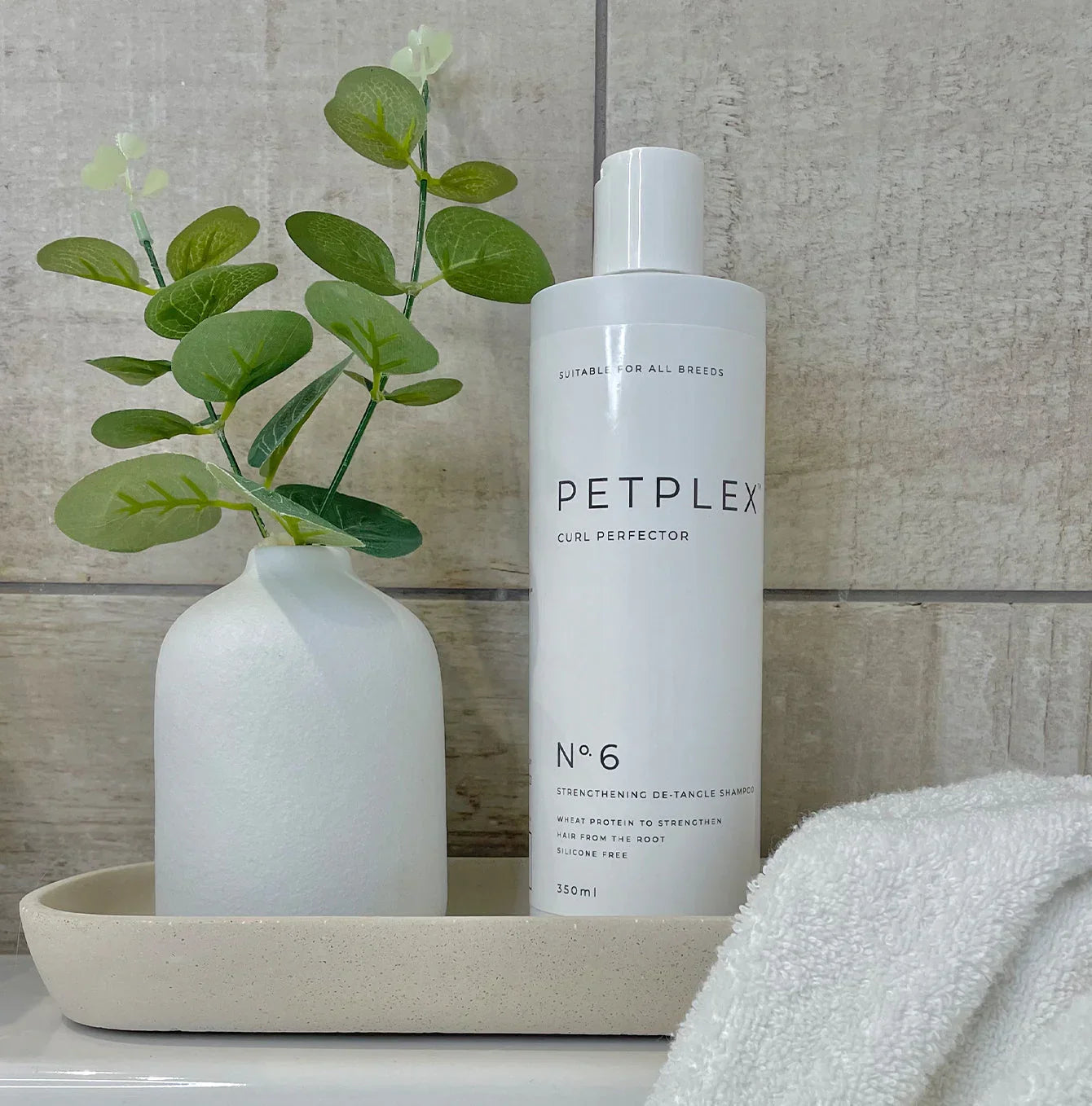 PetPlex No. 6 Curl Perfector Strengthening De-Tangle Shampoo displayed on a bathroom tray with a towel and decorative vase