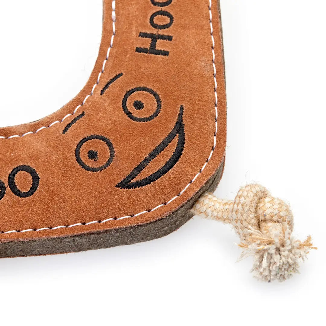 A brown eco dog toy resembling a boomerang with a smiley face on the corner made of jute and suede on a white background.