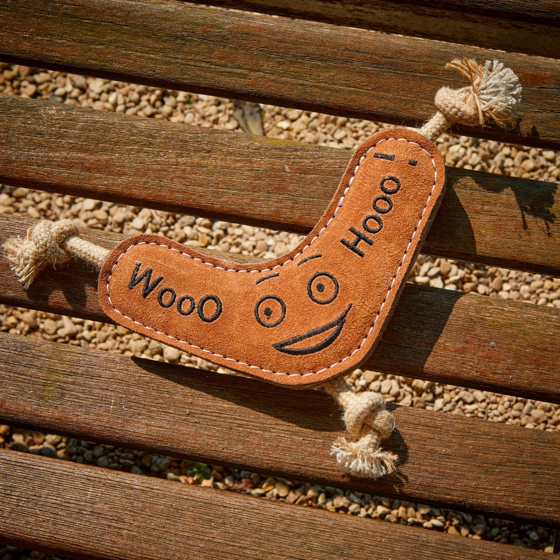 Jute and suede eco dog toy resembling a boomerang with 'WooO' and 'HooO' text laid on a wooden surface.