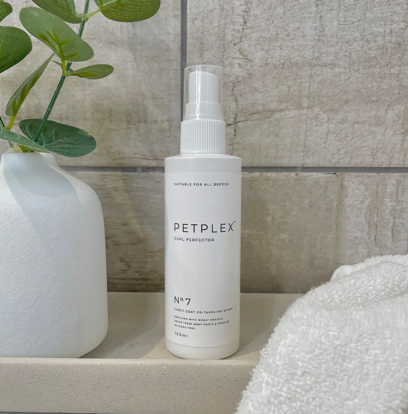 Petplex curly coat dog detangler bottle on a shelf with a plant and towel