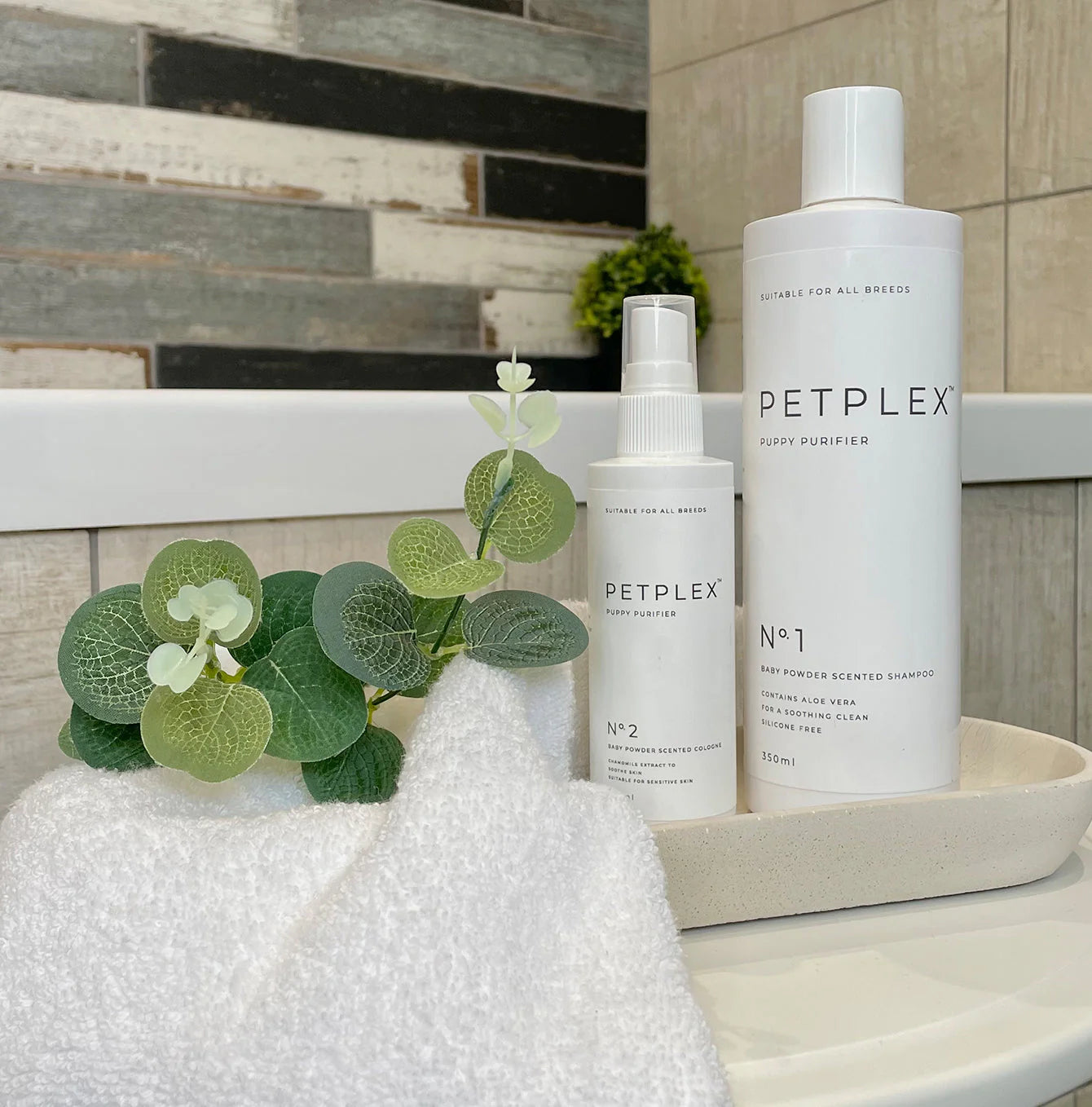 PetPlex puppy shampoo and cologne set on a bathroom counter with a towel and plant.